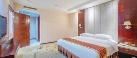 A hotel room with a large bed, a television, a wooden wardrobe, and a red accent wall.