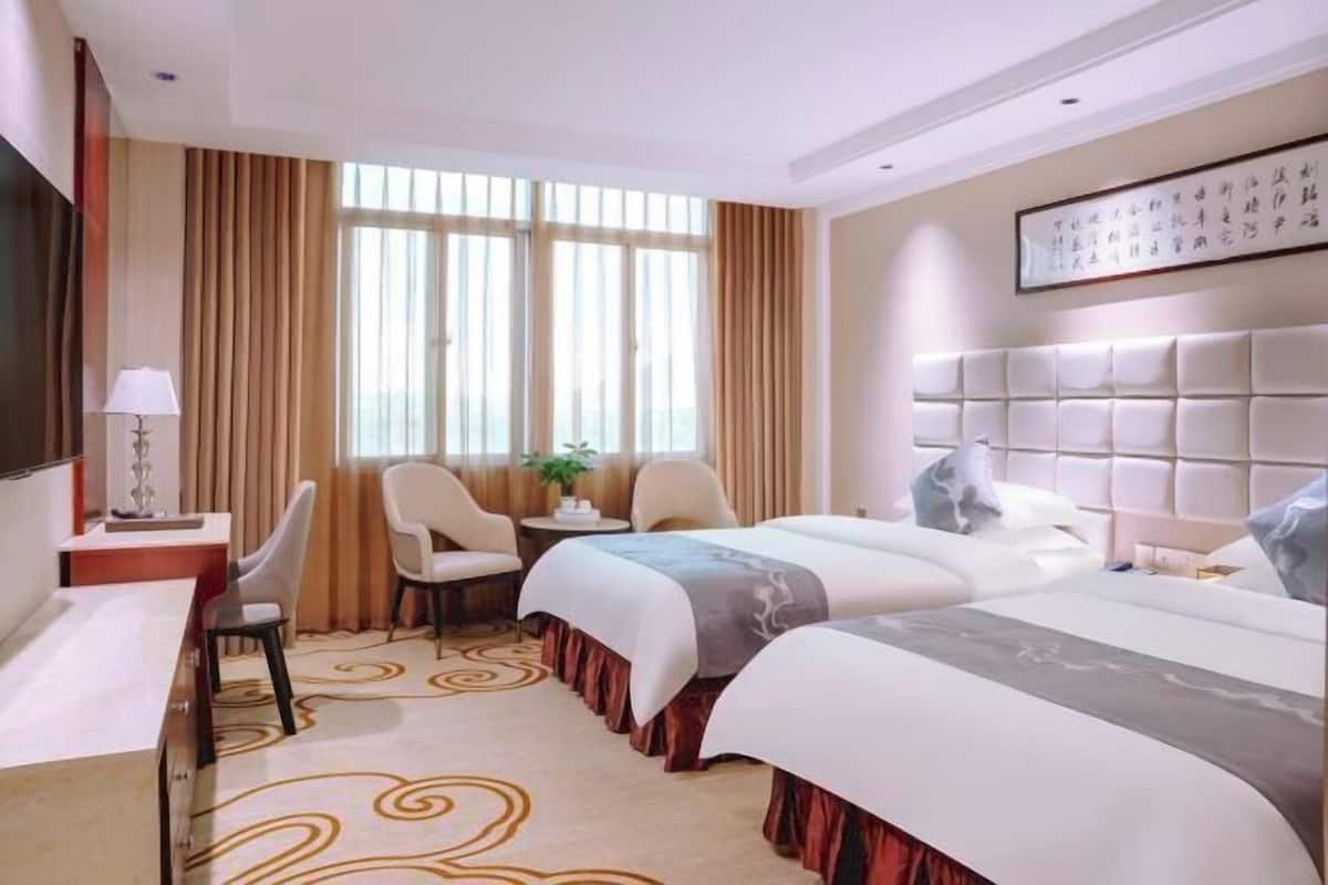 A hotel room with two beds, a desk, a chair, and a large window with curtains.