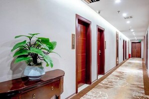 Un pasillo de hotel con una planta en maceta, puertas de madera y una alfombra estampada.