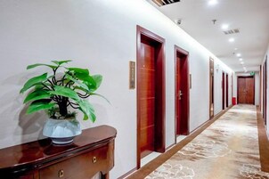 A hotel hallway with a potted plant, wooden doors, and a patterned carpet.