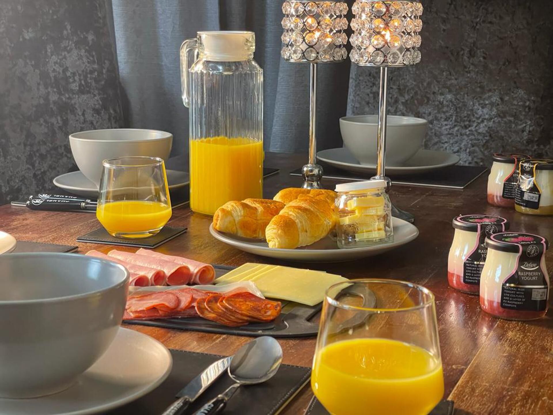 Una mesa de desayuno con croissants, queso, jamón y diferentes condimentos.