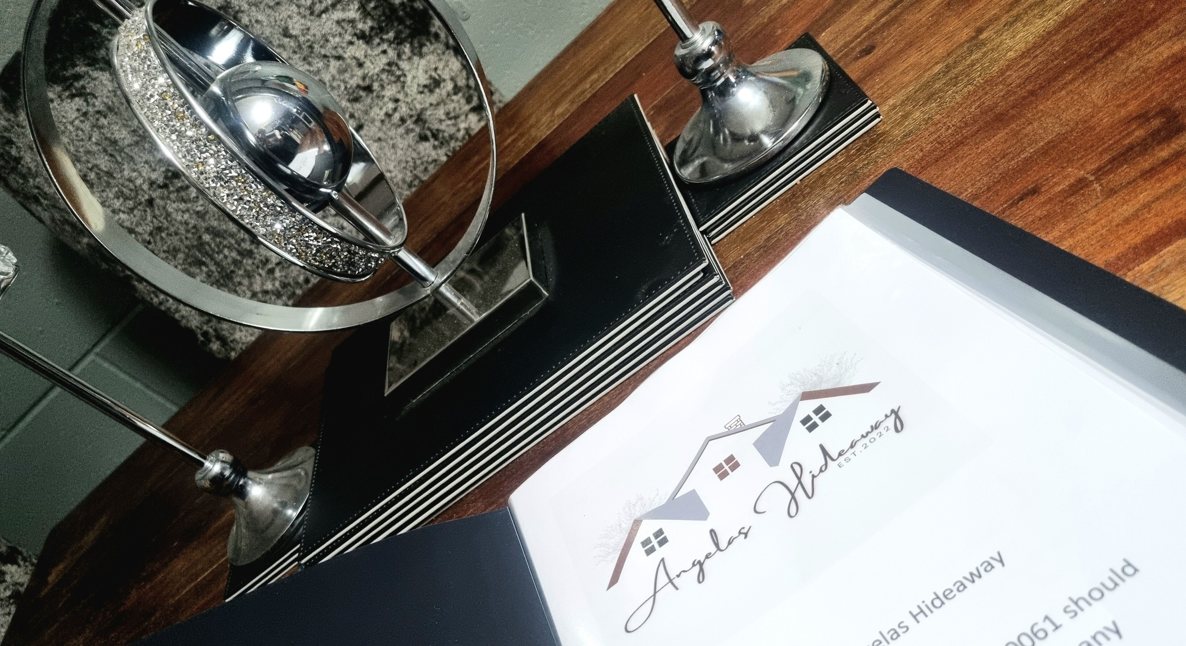 A black metal stand with a glass object on it, possibly a decorative item, and a white card with the text "Angelas Hideaway" and a logo.