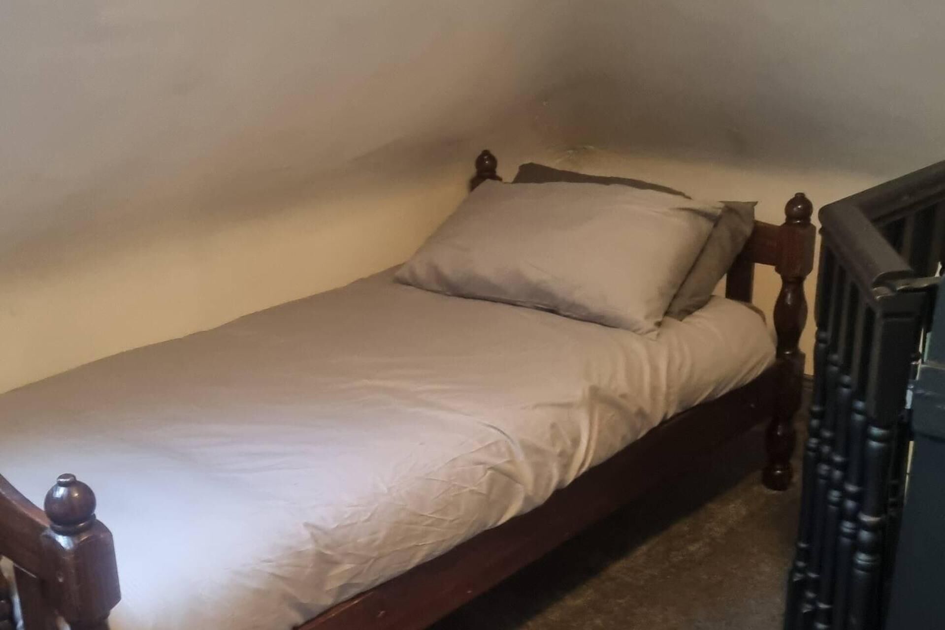 A small, single-bed room with a wooden headboard and a simple white bedspread.