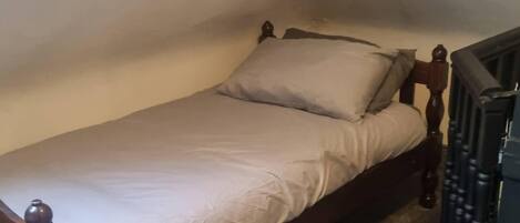A small, single-bed room with a wooden headboard and a simple white bedspread.