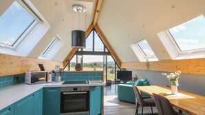 A modern kitchen with a large island, a dining area with a wooden table, and a view of the outdoors through a skylight. - Kerry Hill - The Sheepfold (Llandrindod Wells)