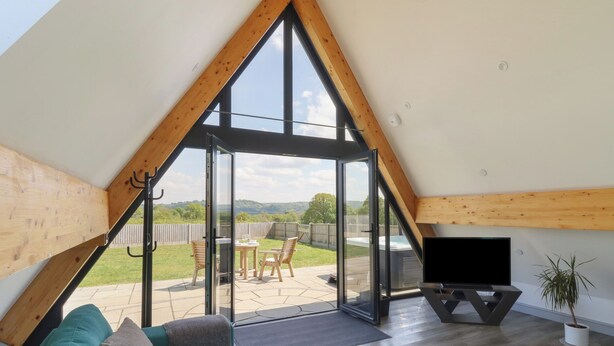 A spacious loft bedroom with a large skylight, a cozy seating area with a sofa, and a TV on a stand. - Kerry Hill - The Sheepfold (Llandrindod Wells)