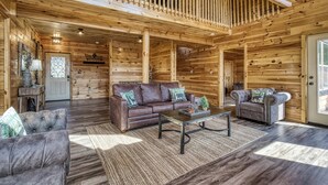Uma cabana de madeira espaçosa com um quarto no mezanino, uma sala de estar com sofá de couro marrom e uma área de jantar com mesa de centro.