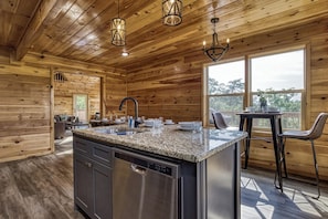 A kitchen with wooden walls, a granite countertop, stainless steel appliances, and a dining area with chairs and a table.