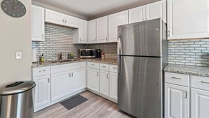 A kitchen with white cabinets, a stainless steel refrigerator, a microwave, and a clock on the wall.