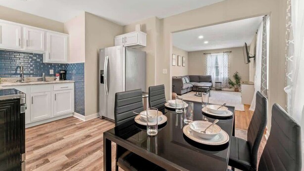 A modern kitchen with white cabinets, a blue-tiled backsplash, and a dining area with a black table and chairs.