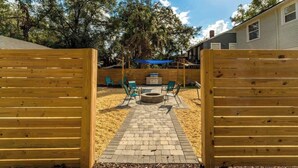 A backyard with a brick pathway leading to a fire pit surrounded by chairs.
