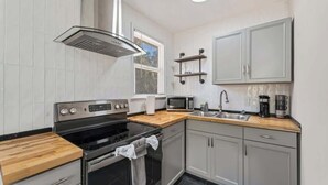 A modern kitchen with a stove, oven, microwave, and sink. There are wooden countertops and grey cabinets. - Flagler Haus 1539 - TV, AC, WiFi (Jacksonville)
