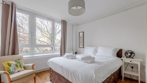 Une chambre à coucher avec un grand lit, une chaise, une table de chevet et une fenêtre avec des rideaux.