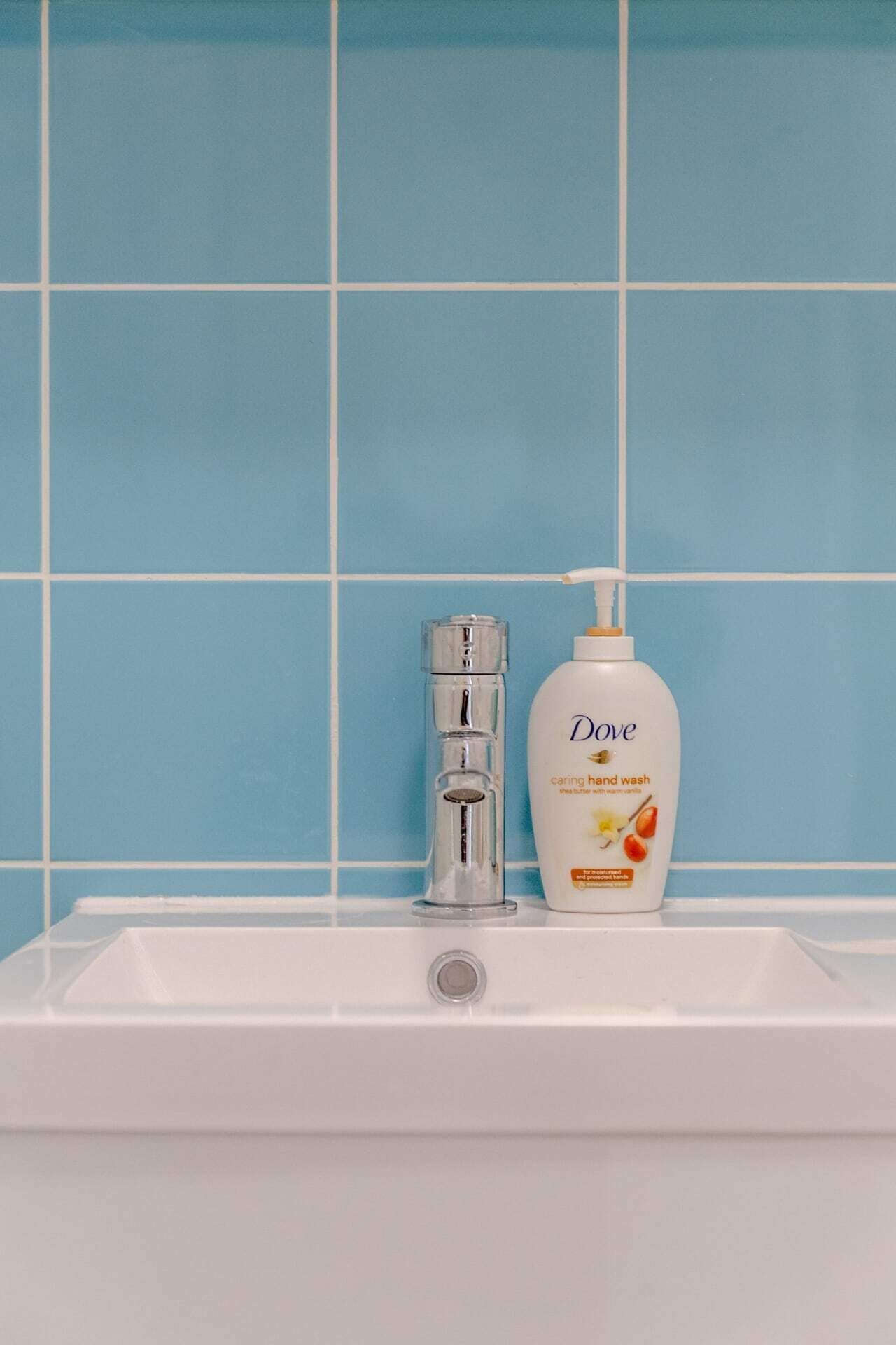 Un bagno con un lavandino bianco, un erogatore di sapone e un rubinetto su una parete rivestita di piastrelle blu.