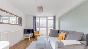 Un salon moderne avec un canapé gris, un fauteuil jaune, une table basse blanche et un téléviseur posé sur un meuble blanc.