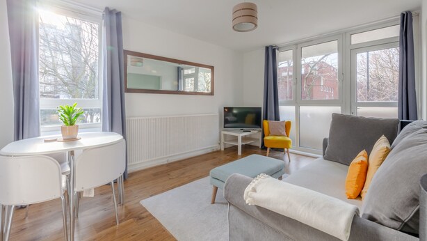 Un salon moderne avec un canapé, un pouf, une télévision et une petite table sur laquelle est posée une plante.