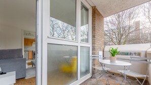 Un appartement moderne doté d’un balcon, d’un coin repas avec une table et des chaises, et d’une cuisine en arrière-plan.