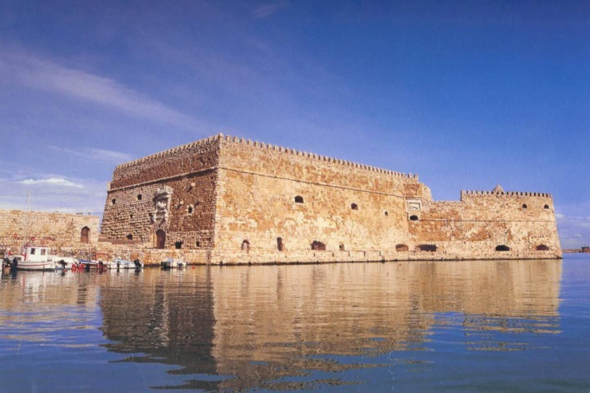 A historic stone fortress with a moat, featuring a large central tower and multiple smaller towers along the walls.