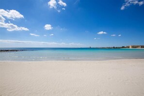 A beach with clear blue water and a sandy shore.