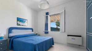 Une chambre à coucher comprenant un lit, une table de chevet, une fenêtre avec des rideaux, un radiateur et un tableau accroché au mur.