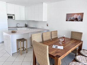 Eine moderne Küche mit weißen Schränken, einer Mikrowelle und einem Essbereich mit einem Holztisch und Korbstühlen.