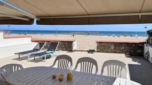 An outdoor seating area with a table and chairs, overlooking a beach with umbrellas and people. - On the beach (Valras-Plage)