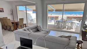 A modern living room with a grey sofa, a laptop, and a dining area with wicker chairs. - On the beach (Valras-Plage)