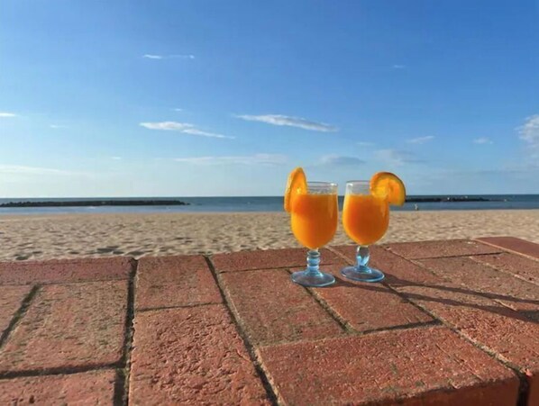 Zwei Gläser Orangensaft auf einem Ziegelvorsprung, im Hintergrund ein Strand und ein Meer.