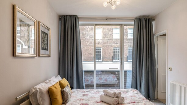 Une chambre à coucher avec un lit, une fenêtre avec des rideaux, un radiateur et des tableaux encadrés accrochés au mur.