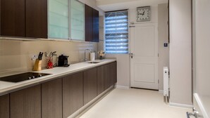 Une cuisine moderne avec des meubles de couleur bois foncé, un plan de travail blanc, une cuisinière encastrée et une fenêtre avec des stores.