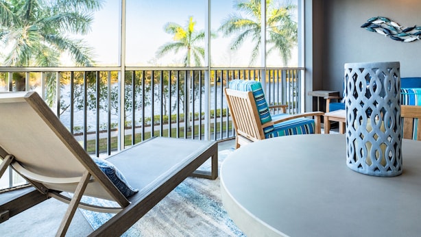 Habitación iluminada por el sol con vistas a palmeras, una mesa redonda y una silla con cojín a rayas.