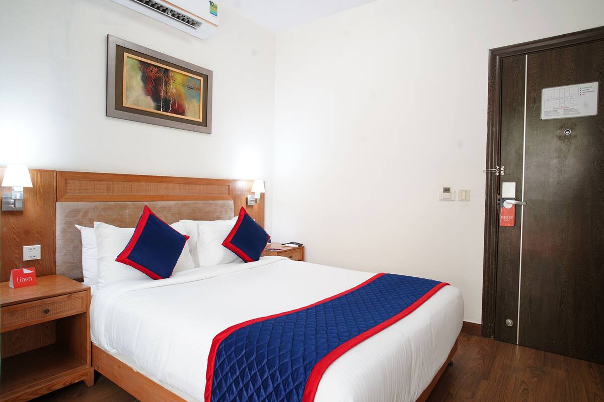A hotel room with a large bed, wooden headboard, white bedding, and a blue quilted throw.