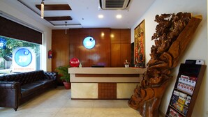 A hotel reception area with a wooden reception desk, a leather sofa, a large potted plant, and a wall-mounted sign. - Zip By Spree Hotels Delhi Greater Kailash (New Delhi)
