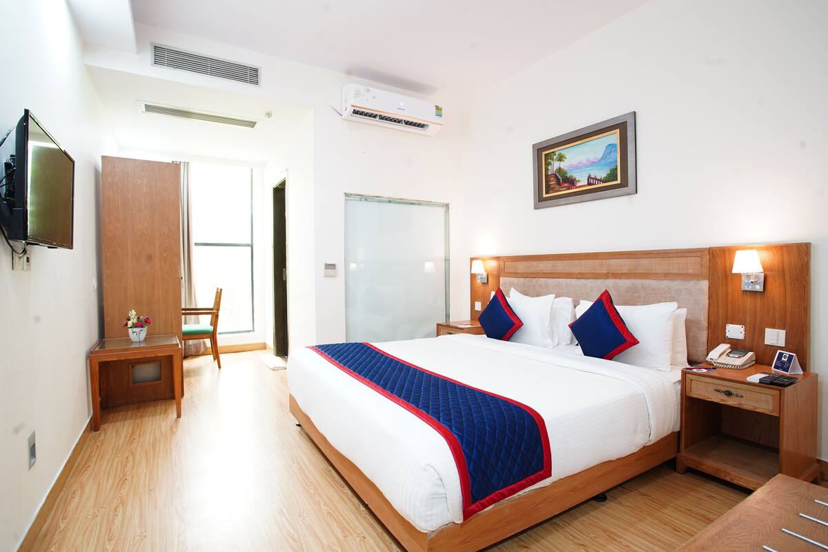 A hotel room with a large bed, bedside tables, a desk, a chair, and a television.
