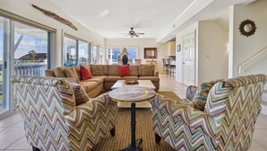 Un salon spacieux avec un grand canapé d’angle, une table basse ronde et un ventilateur de plafond.