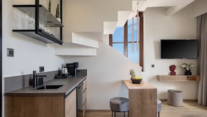 A modern kitchen with a wooden countertop, a coffee machine, and a bowl of fruit. There is a staircase leading to a balcony with a view of the sky. - Ethos Suites (Chania)