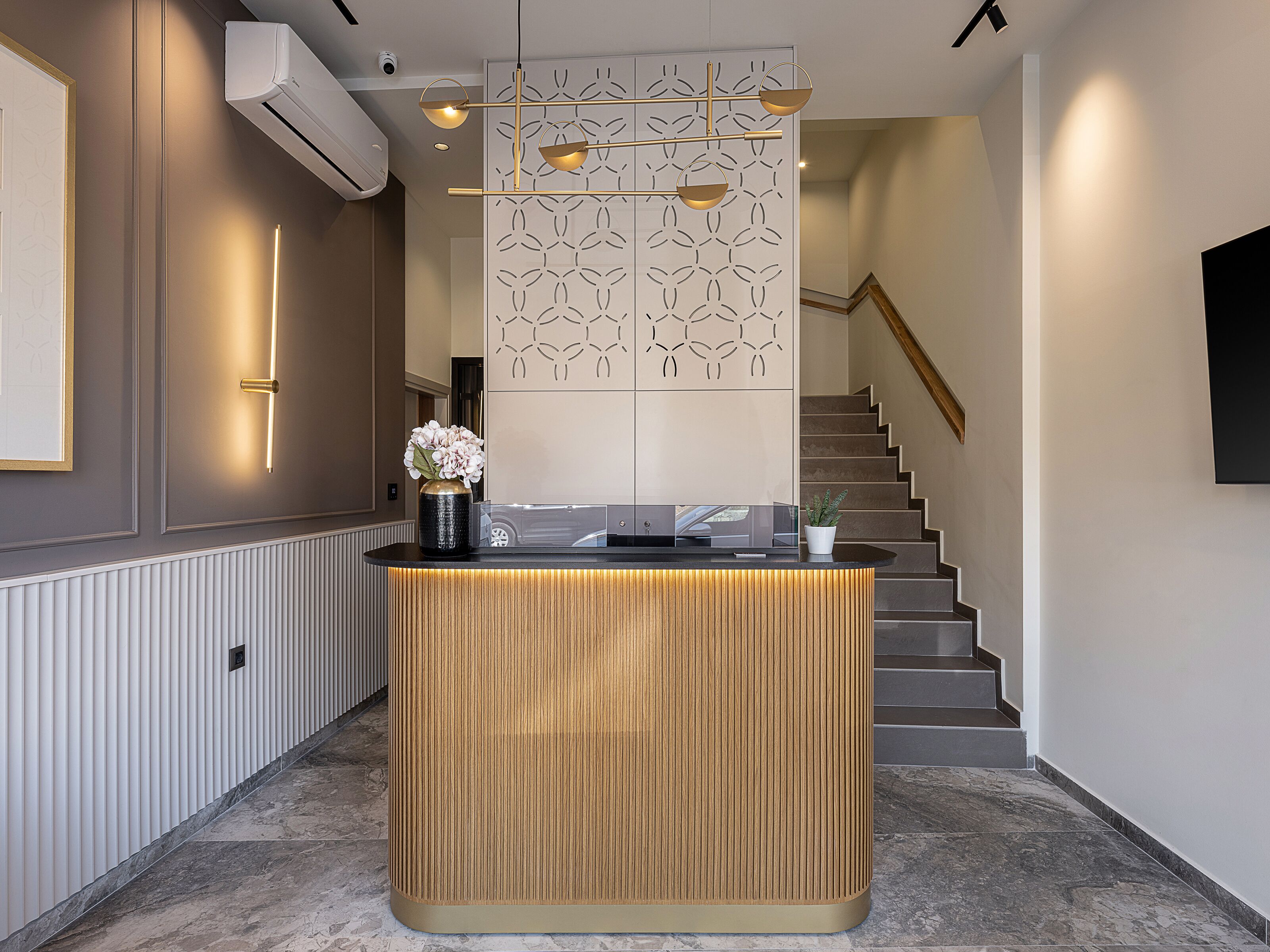 A reception desk with a wooden finish, a vase with flowers, and a modern light fixture above.