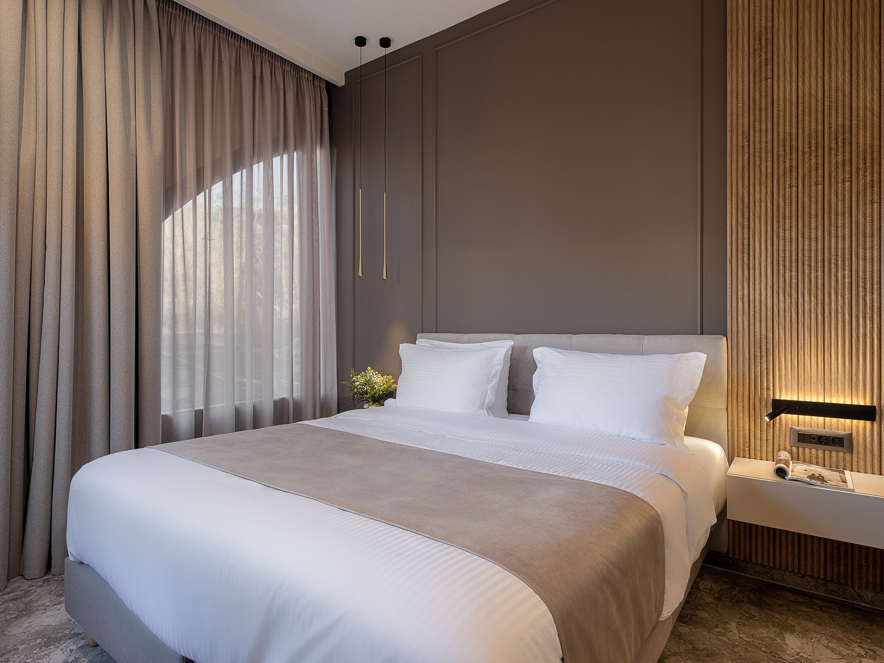 Une chambre d’hôtel moderne avec un grand lit, une table de chevet et une lampe fixée au mur.