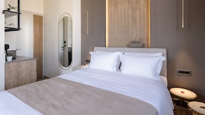 A modern bedroom with a large bed, a bedside table, a mirror, and a wall-mounted light fixture. - Ethos Suites (Chania)