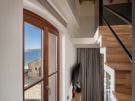 Un interior moderno con un gran ventanal que ofrece vistas al mar, una escalera de escalones de madera y un televisor de pantalla plana montado en la pared.