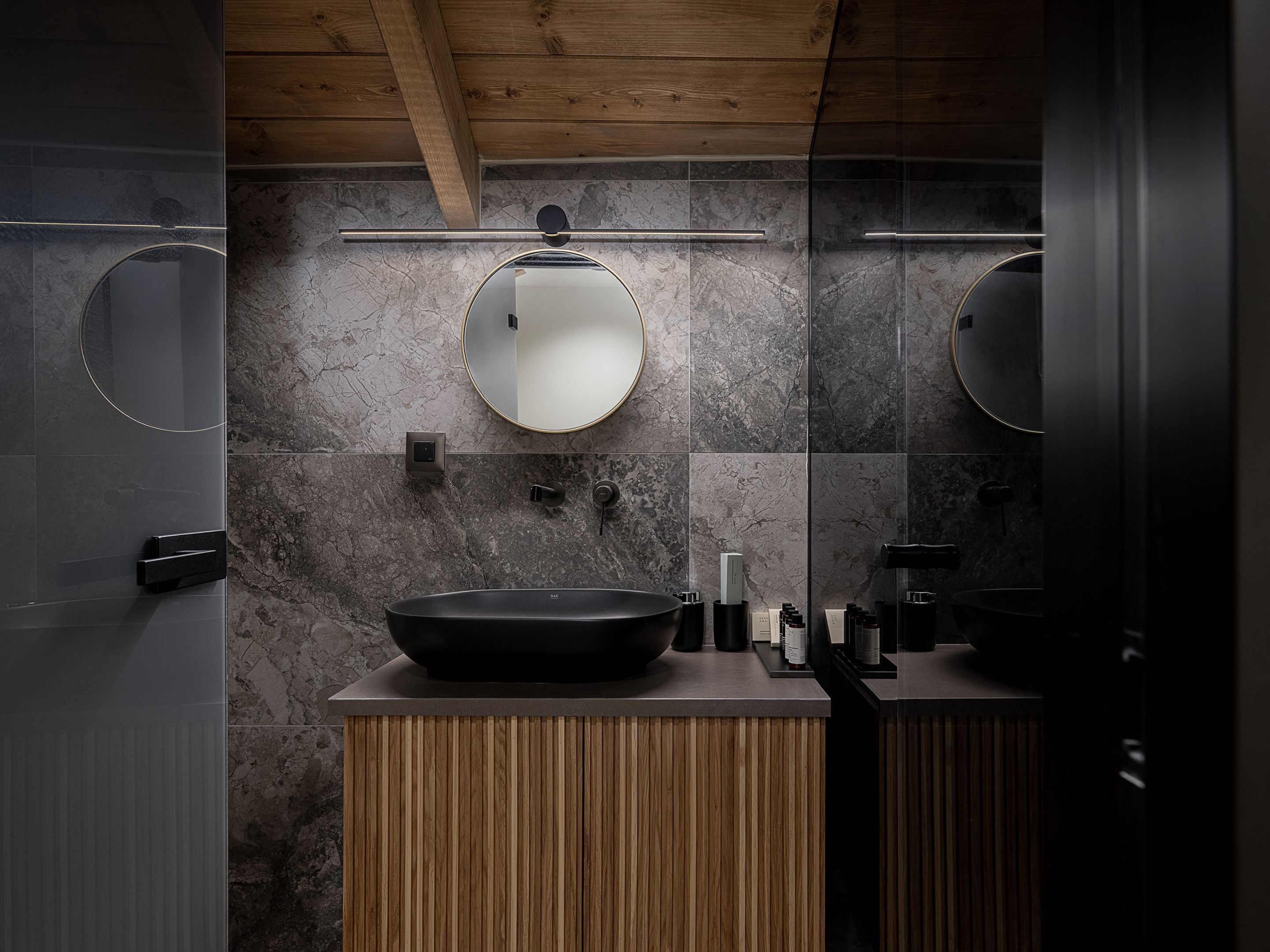 A modern bathroom with a wooden vanity, a large mirror, and a black sink.