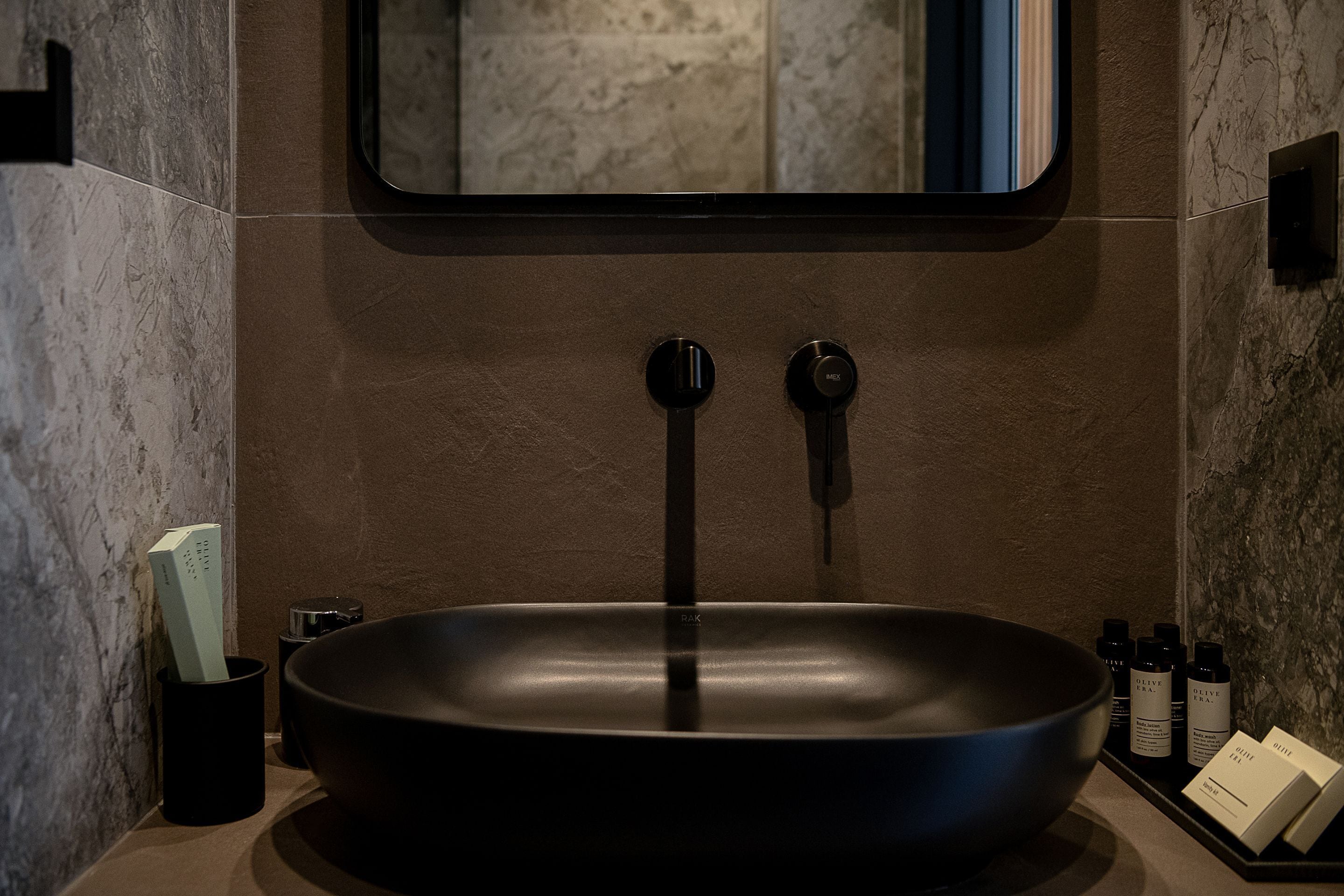 A modern bathroom with a large, dark-colored vessel sink, a mirror above it, and toiletries on the side.