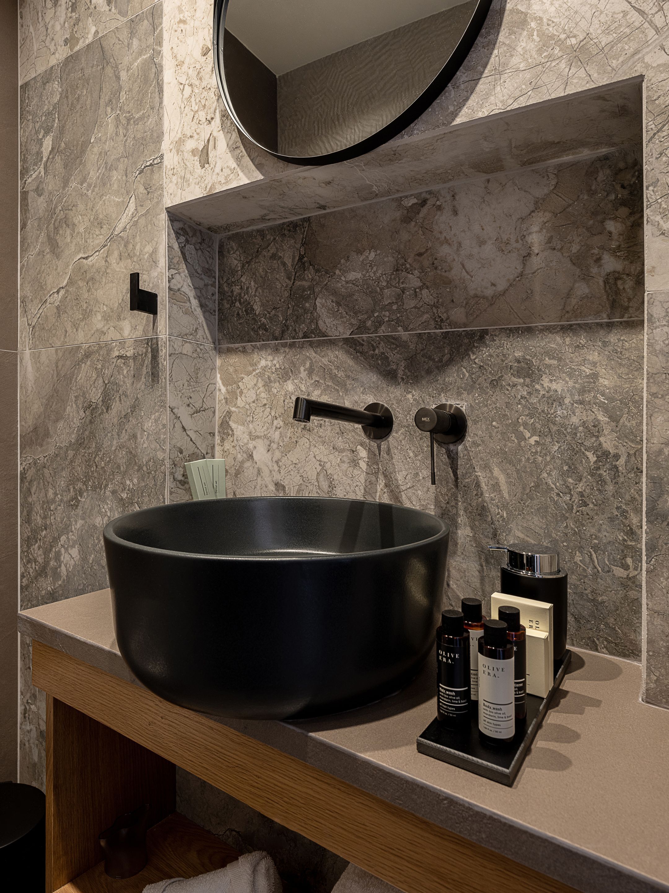 Un baño moderno con un lavamanos negro grande, un espejo redondo y un salpicadero de mármol.