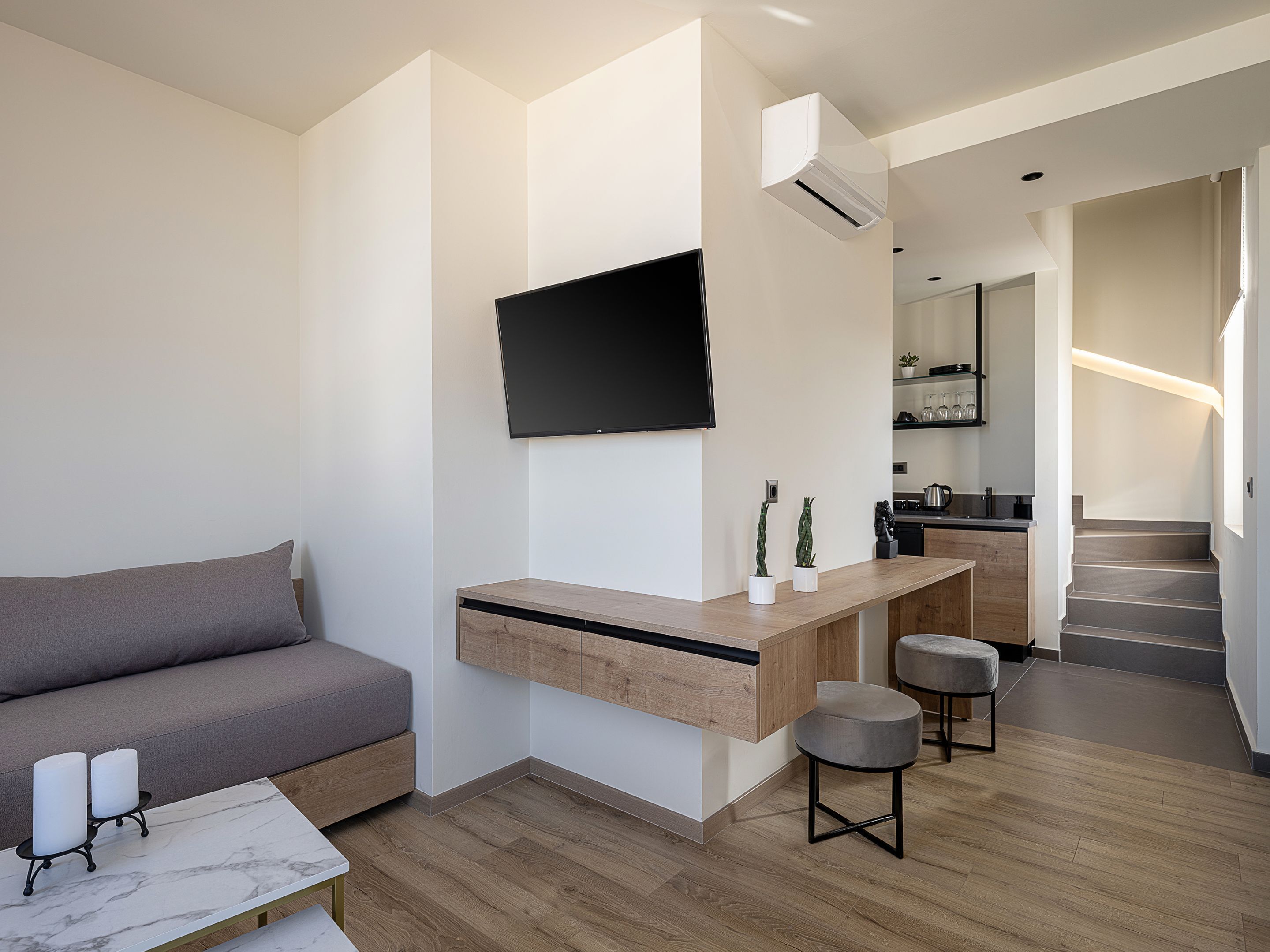 A modern living room with a sofa, a coffee table, a TV mounted on the wall, and a kitchen area in the background.