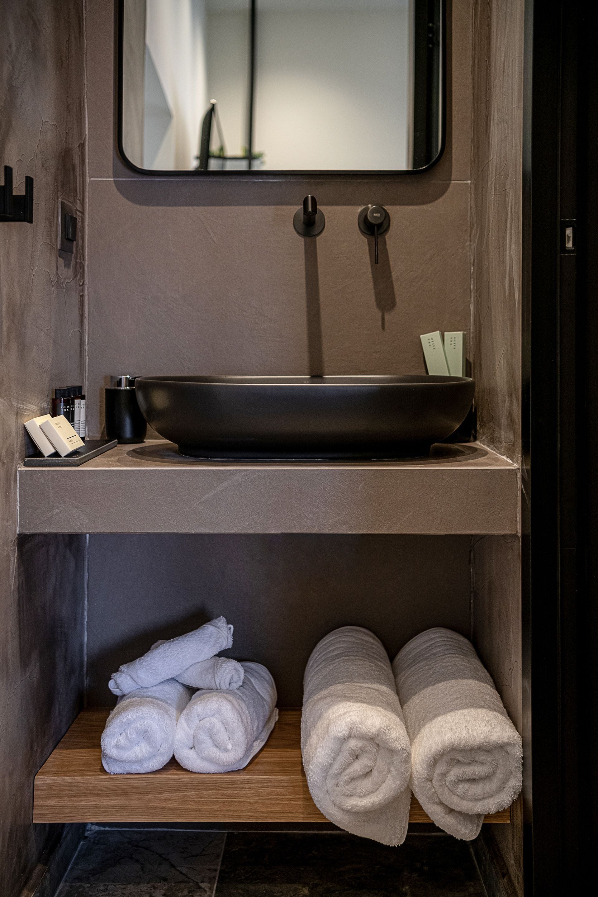 A bathroom with a black sink, a mirror, and a shelf with rolled towels.