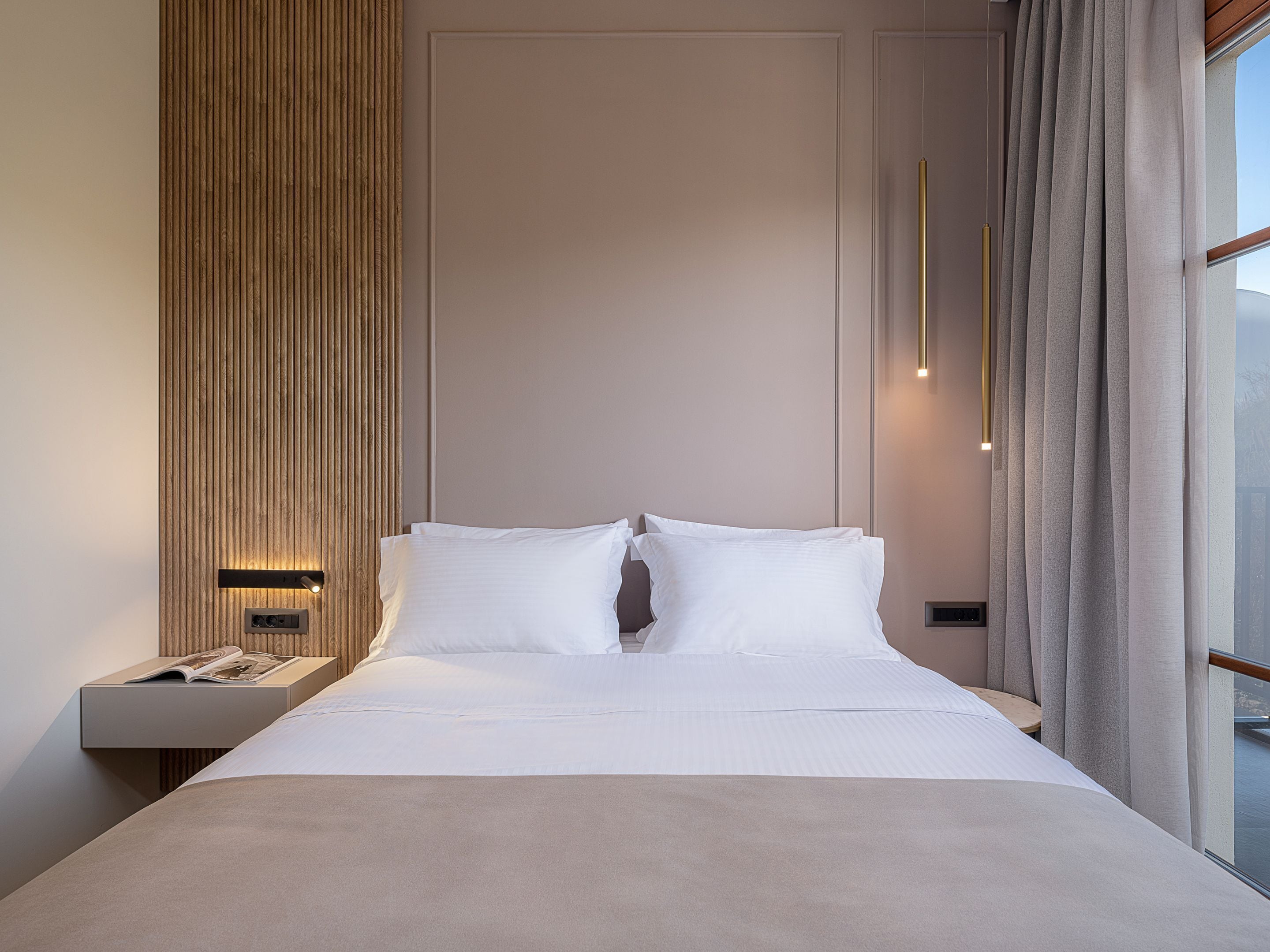 Habitación de hotel moderna con una cama grande, una pared decorativa de madera, una mesita de noche con lámpara y vistas al exterior.
