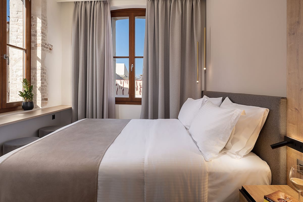 A neatly made bed with white linens, a wooden headboard, and a bedside table with a glass of wine and a book.