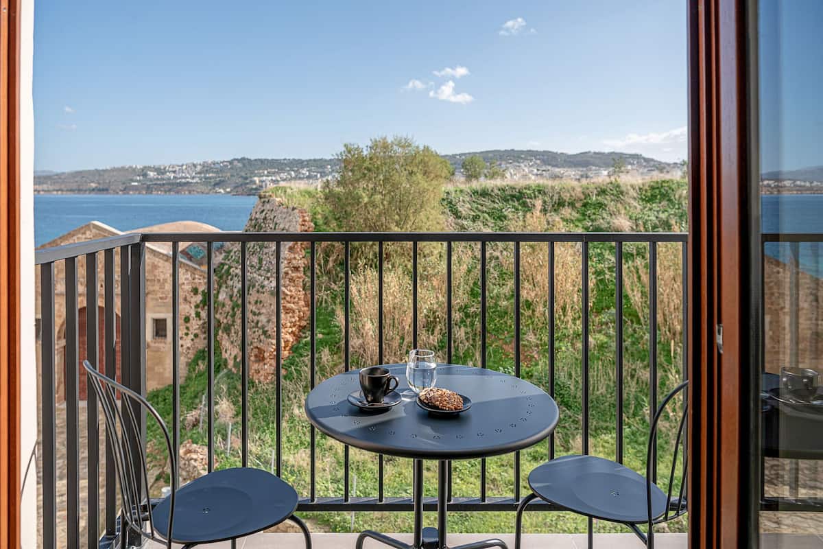 A balcony with a round table, two chairs, a cup, and a glass of water.
