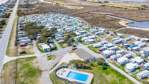 Luchtbeeld van een camping met campers en stacaravans, een zwembad en een weg ernaast.