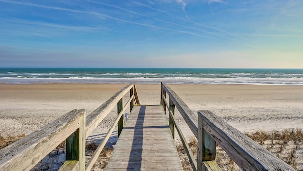 Een houten looppad dat naar een strand leidt, met een heldere lucht.